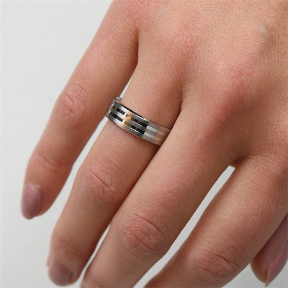 Een hand met een Boccia Titanium Ring 0101-02 in zilver en zwarte strepen op de middelvinger. De natuurlijke, ongepolijste nagels steken af tegen een effen witte achtergrond en benadrukken dit tijdloze accessoire.