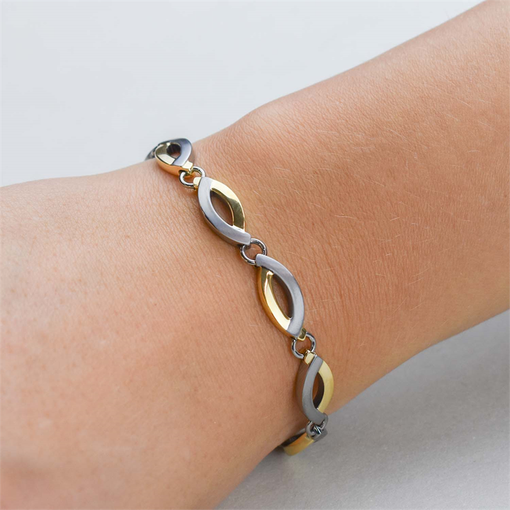 Een close-up van een pols met de Boccia Titanium Armband Bicolor 03001-02, met afwisselend gouden en zilveren ovale titanium schakels van Boccia, tegen een lichte, neutrale achtergrond.