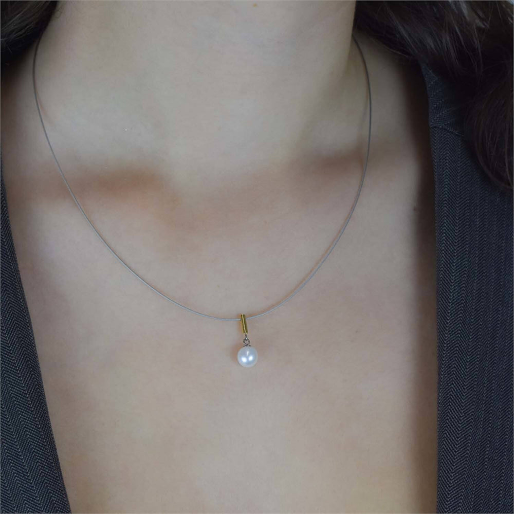 Een close-up van een persoon die de Boccia Titanium Collier Parel Bico st 08036-02 draagt: een slanke ketting met een enkele witte parel als hanger, stijlvol gecombineerd met een donker topje met V-hals.