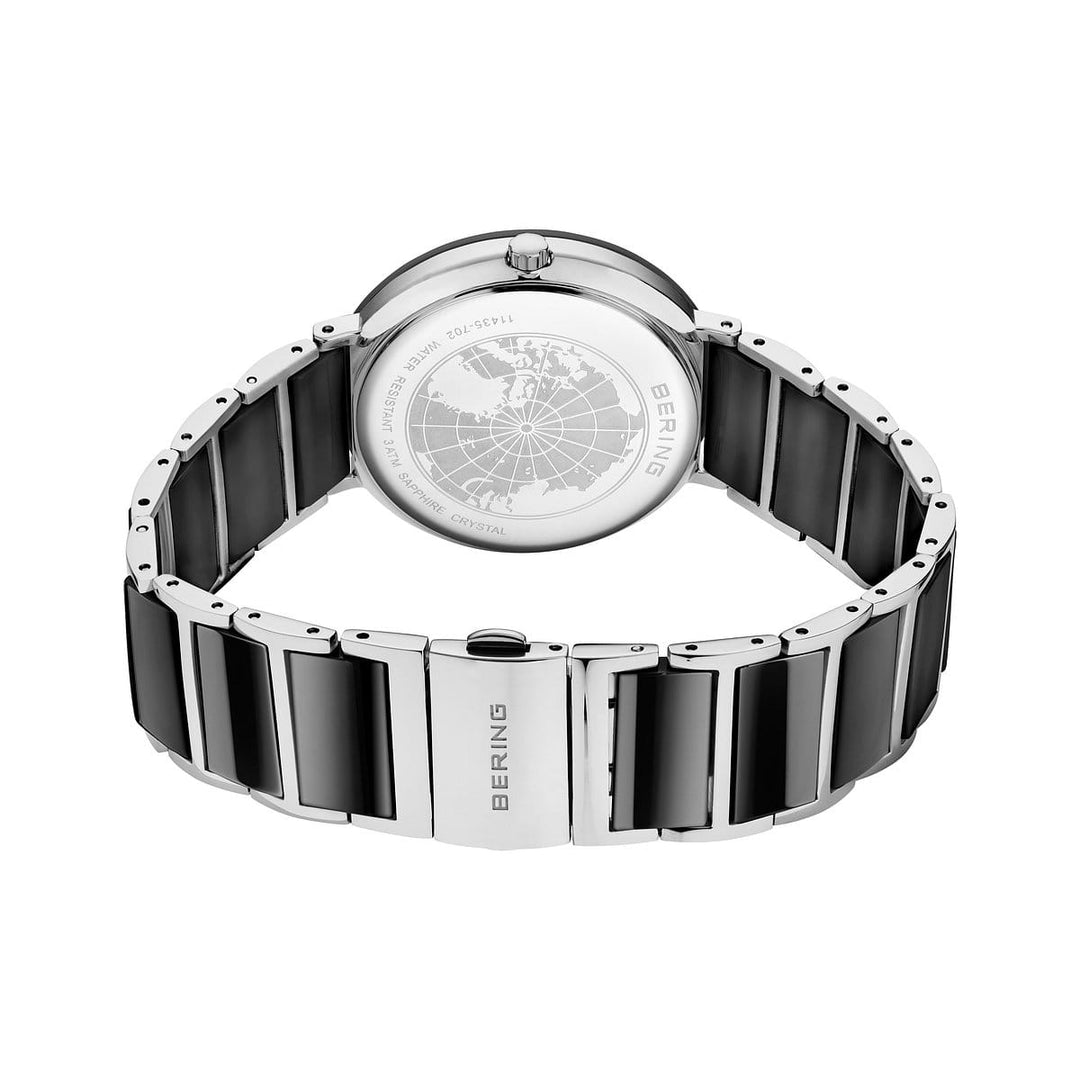 De Bering 11435-702 dameshorloge in zilver en zwart wordt getoond met de gegraveerde achterkant van de wereldkaart en merkdetails, plus een metalen armband met het Bering-logo op de sluiting voor een luxe uitstraling.