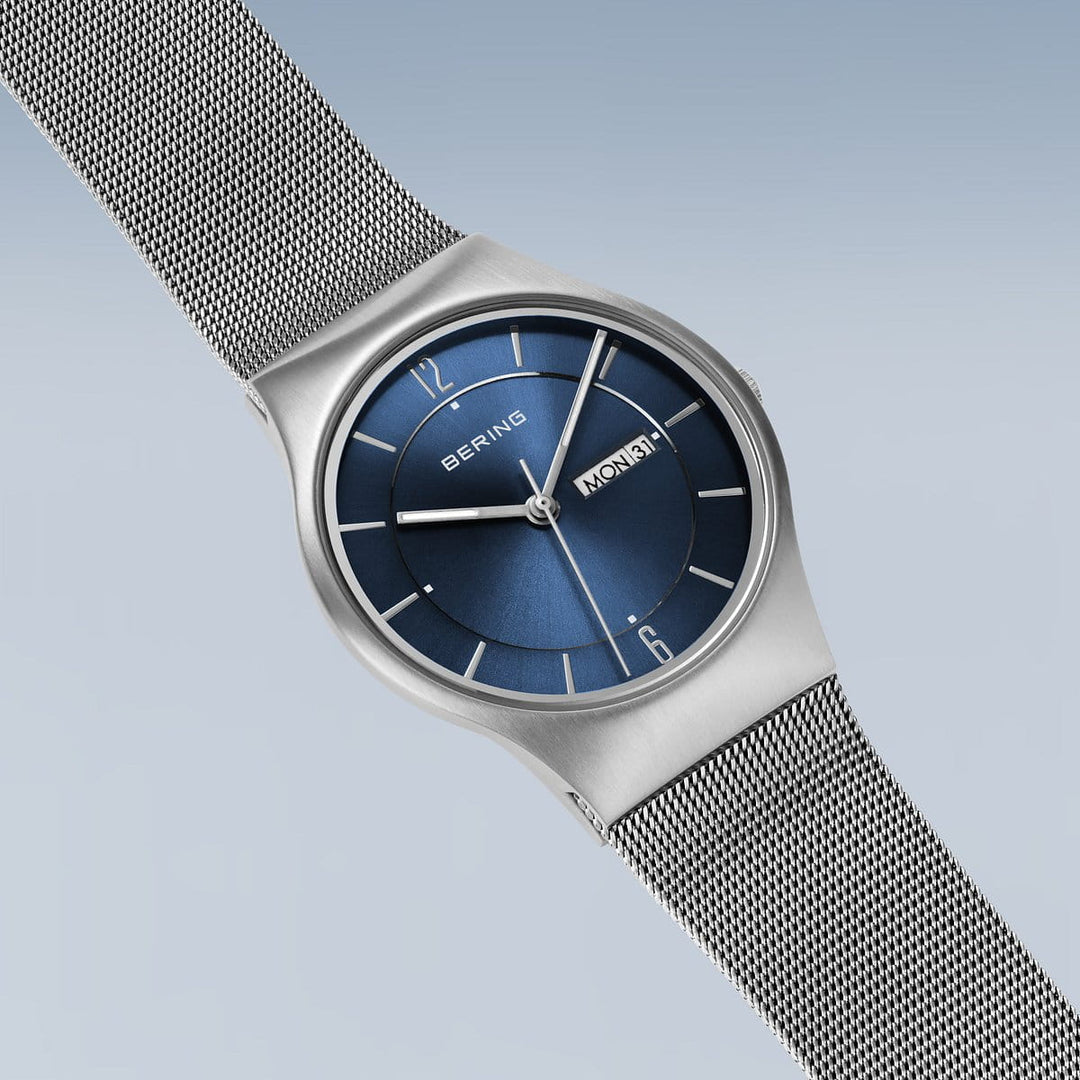 De Bering 11938-003DD is een strak, minimalistisch horloge met een blauwe wijzerplaat, zilveren mesh band en duurzaam saffierglas. Het quartz uurwerk zorgt voor precisie, met eenvoudige uurmarkeringen en een dagweergave op de stijlvolle blauwe achtergrond met kleurverloop.