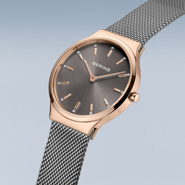 Het Bering horloge, model 12131-339-GWP, heeft een roségouden kast en een Milanees band. Het beschikt over een elegante minimalistische donkere wijzerplaat met precieze uurmarkeringen, Quartz-uurwerk uurwerk en de merknaam BERING op een zachte gradiëntachtergrond.