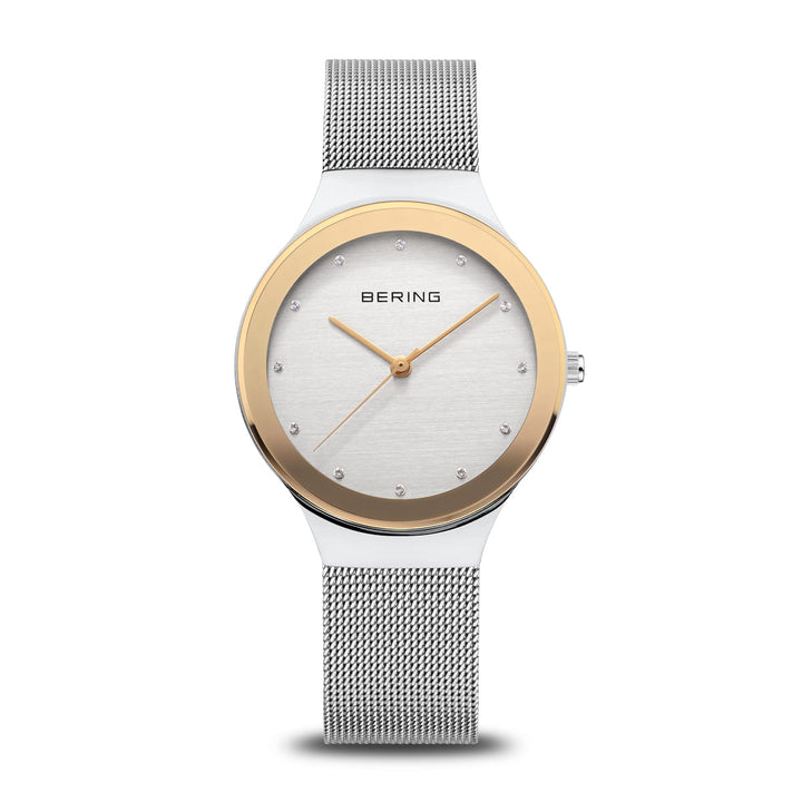 Berings 12934-010 Dameshorloge toont een tijdloos design met een zilveren meshband, ronde wijzerplaat, roestvrijstalen kast, gouden lunette, minimalistische uurmarkeringen en twee wijzers. Bering is elegant gepositioneerd onder de 12-uursmarkering.