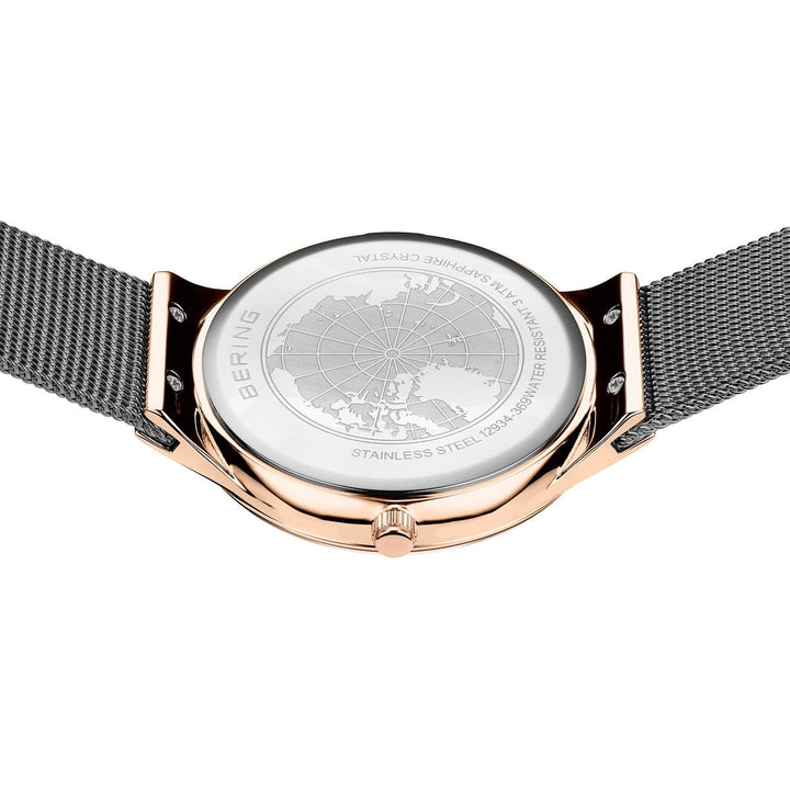 De Bering 12934-369 heeft een roestvrijstalen meshband met roségouden afwerking en een quartz-uurwerk. De achterkant toont een ingewikkeld gegraveerde wereldkaart, met etsen die details over de constructie van roestvrij staal en saffierglas benadrukken.