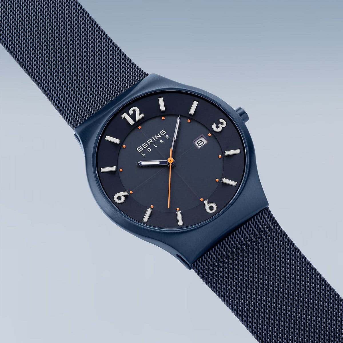 Het Bering-model 14440-393 wordt schuin weergegeven en heeft een blauw zonne-uurwerk en een mesh-band. Het horloge heeft een zwarte wijzerplaat met witte markeringen, een secondewijzer met oranje punt en een klein datumvenster onder duurzaam saffierglas op een achtergrond die van licht naar donkerblauw verloopt.