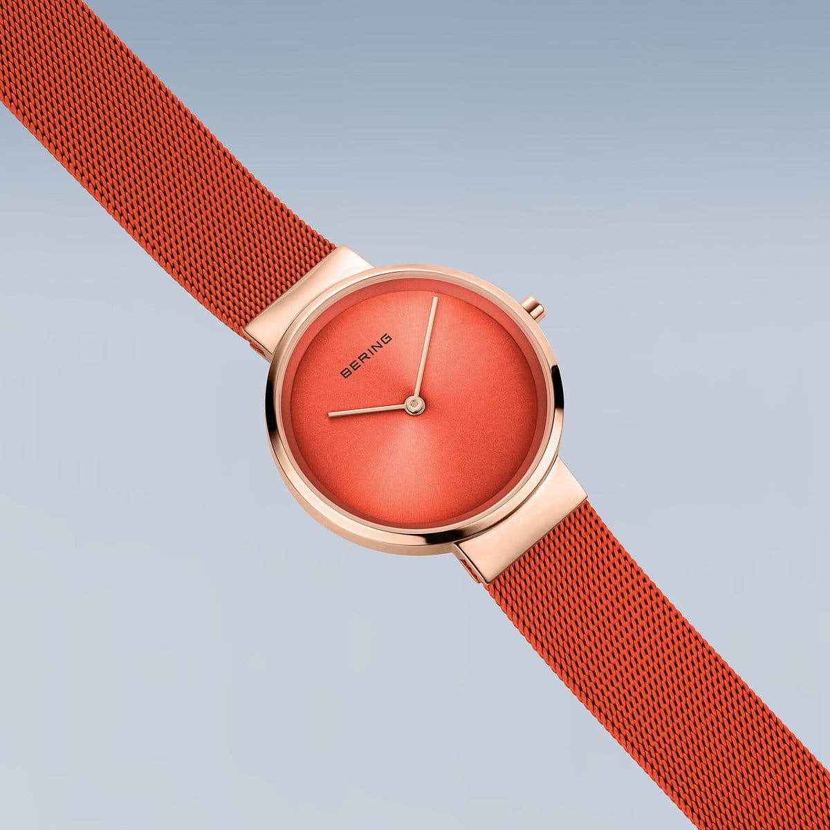Het Bering 14531-565 dameshorloge heeft een roségouden kast en rode wijzerplaat met minimalistische wijzers. De rode meshband contrasteert met de zachtblauwe achtergrond. Dit horloge is met precisie gemaakt en beschikt over quartz-uurwerk en duurzaam saffierglas, wat staat voor tijdloze elegantie.