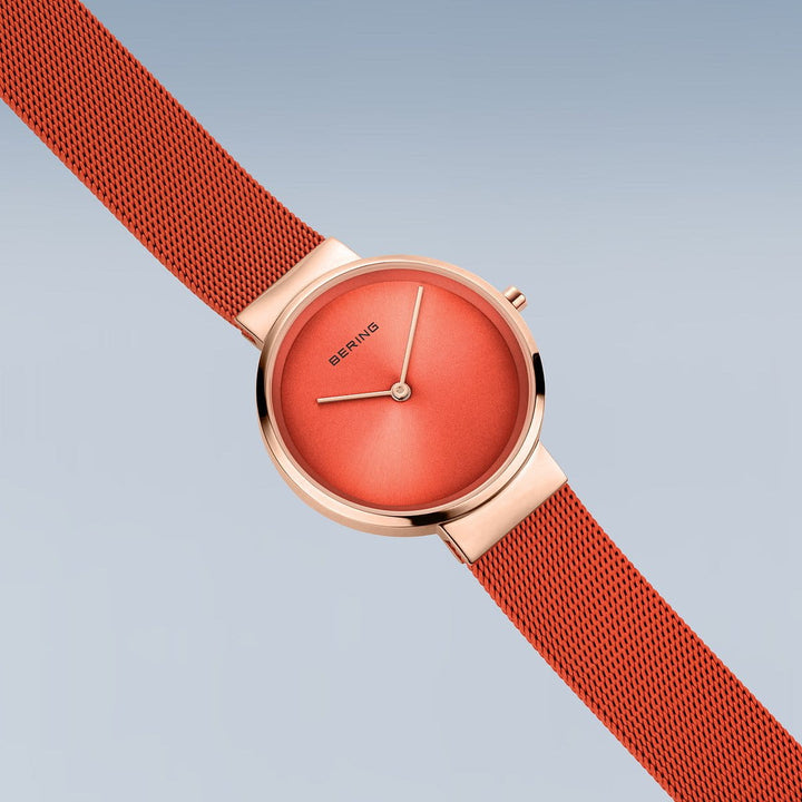 Het Bering 14531-565 dameshorloge heeft een roségouden kast en rode wijzerplaat met minimalistische wijzers. De rode meshband contrasteert met de zachtblauwe achtergrond. Dit horloge is met precisie gemaakt en beschikt over quartz-uurwerk en duurzaam saffierglas, wat staat voor tijdloze elegantie.