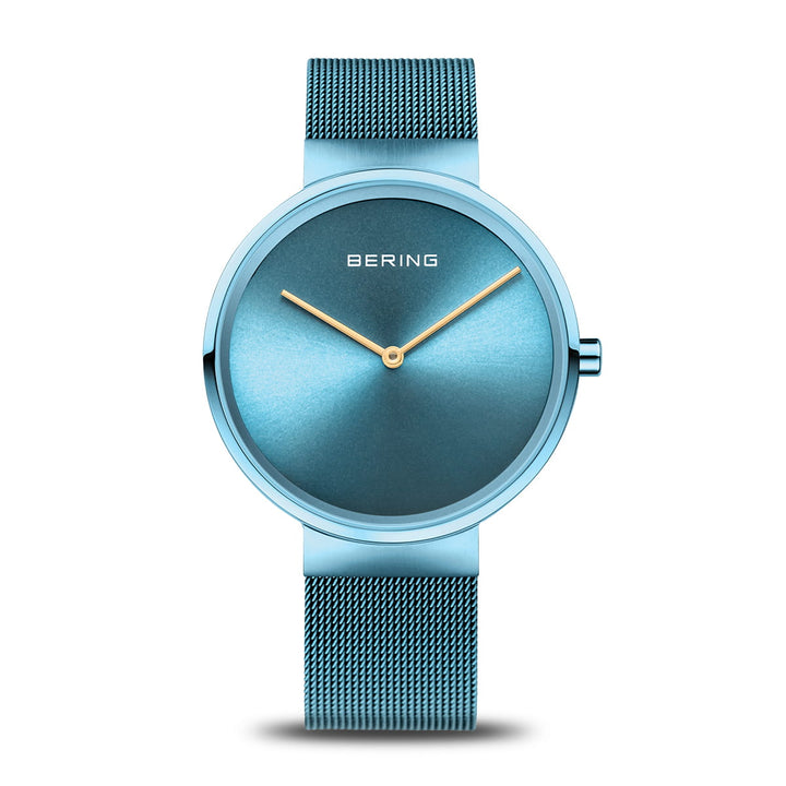 Het Bering dameshorloge 14539-388 heeft een minimalistisch design met een blauwe wijzerplaat, gouden wijzers, quartz-uurwerk, blauwe mesh-band en duurzaam saffierglas, dit alles elegant afgezet tegen een witte achtergrond.