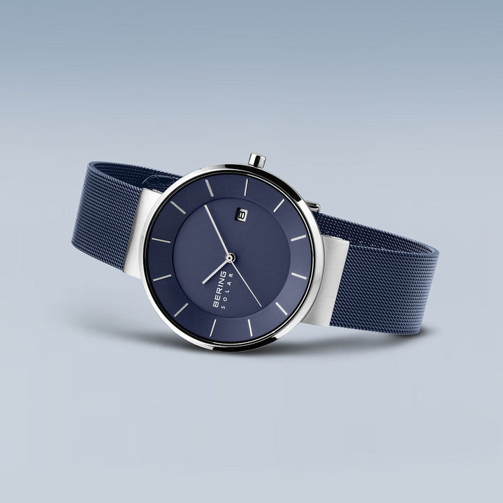 Ontdek het elegante Bering polshorloge 14639-307: een strak horloge met een donkerblauwe wijzerplaat, zilveren uurmarkeringen, datumvenster en eenvoudige wijzers onder robuust Saffierglas. De grijsblauwe meshband belichaamt tijdloze verfijning.