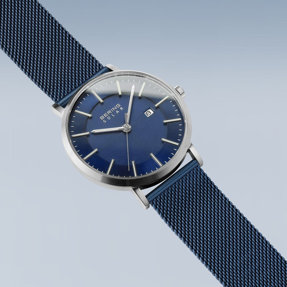 Het Bering 15439-307 Herenhorloge heeft een strak design met een blauwe wijzerplaat, zilveren markeringen op een lichtblauwe achtergrond, duurzaam saffierglas, een datumaanduiding en een moderne blauwe mesh-band.