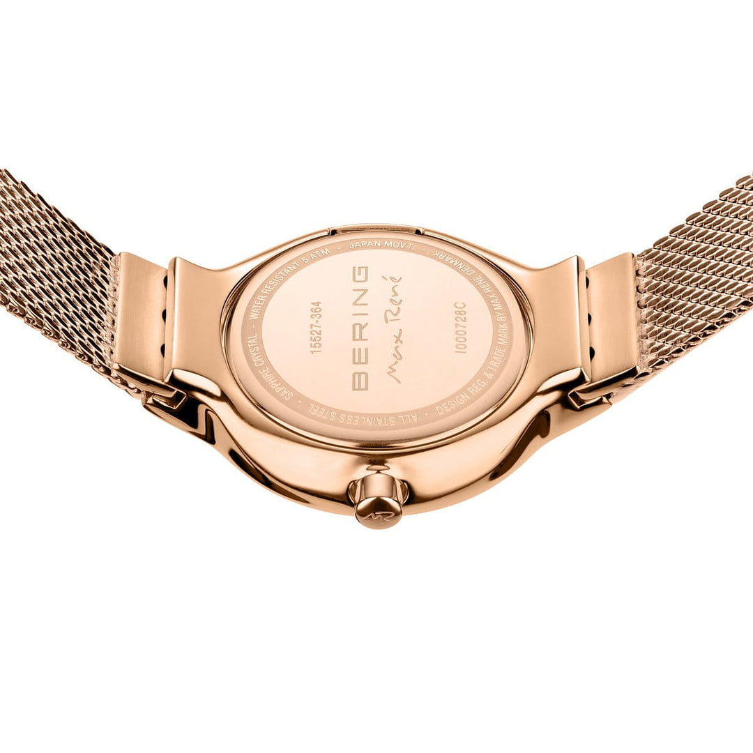 Een close-up van het Bering 15527-364-GWP horloge toont een roségouden mesh band en gegraveerde tekst zoals BERING en een handtekening op de achterkant. Dit quartz-uurwerk heeft een ronde kast, zijkroon en duurzaam saffierglas.