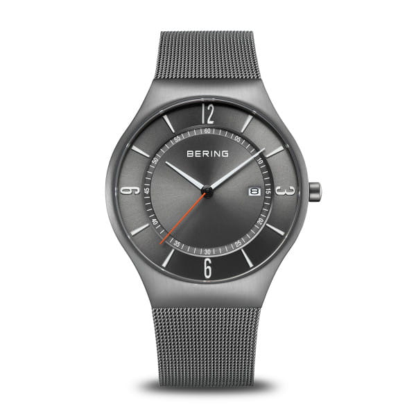 Reloj con esfera gris, correa de malla metálica y detalles en plata, con indicador de fecha.