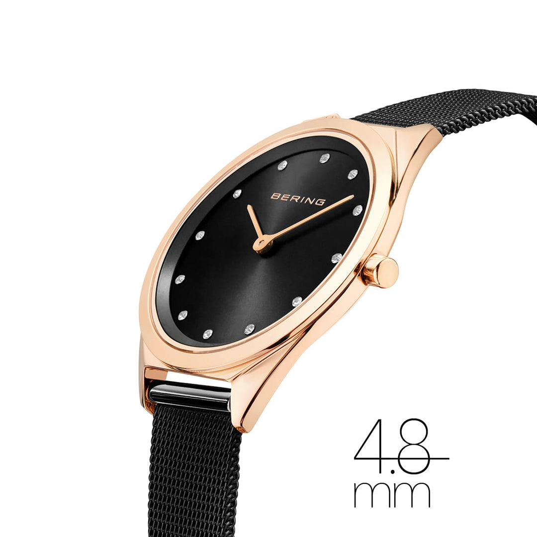 Het Bering 17031-162 Unisex Quartz Horloge heeft een roségouden, krasbestendig saffierglas kast en een zwarte wijzerplaat met sprankelende uurmarkeringen. Het heeft een zwarte mesh band en wordt in een hoek weergegeven om de dikte van 4,8 mm en de roestvrijstalen kast te benadrukken.