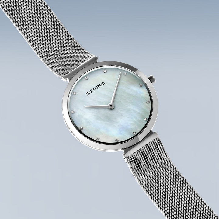 Het elegante dameshorloge, model 18132-004 van Bering, heeft een strakke zilveren meshband en een roestvrijstalen kast. De parelmoeren wijzerplaat bevat diamantachtige markeringen en het merk Bering op 12 uur. Een saffierglas bedekt de zachte gradiëntachtergrond voor tijdloze allure.
