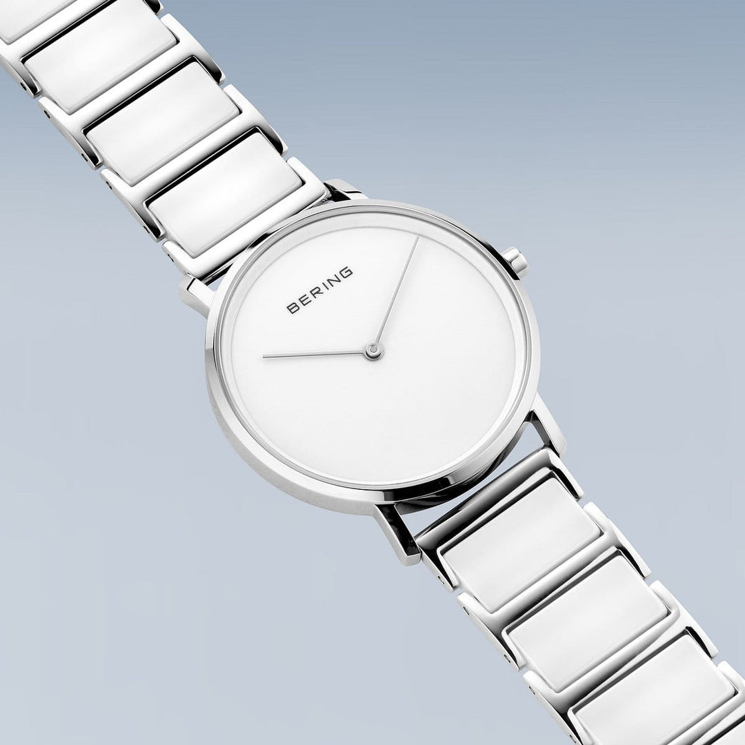 Het Bering dameshorloge 18535-754 heeft een minimalistisch design met een witte wijzerplaat, zilveren metalen band en roestvrijstalen kast. Elegante zilveren uur- en minutenwijzers tegen een lichtblauwe achtergrond laten het merk Bering perfect zien.