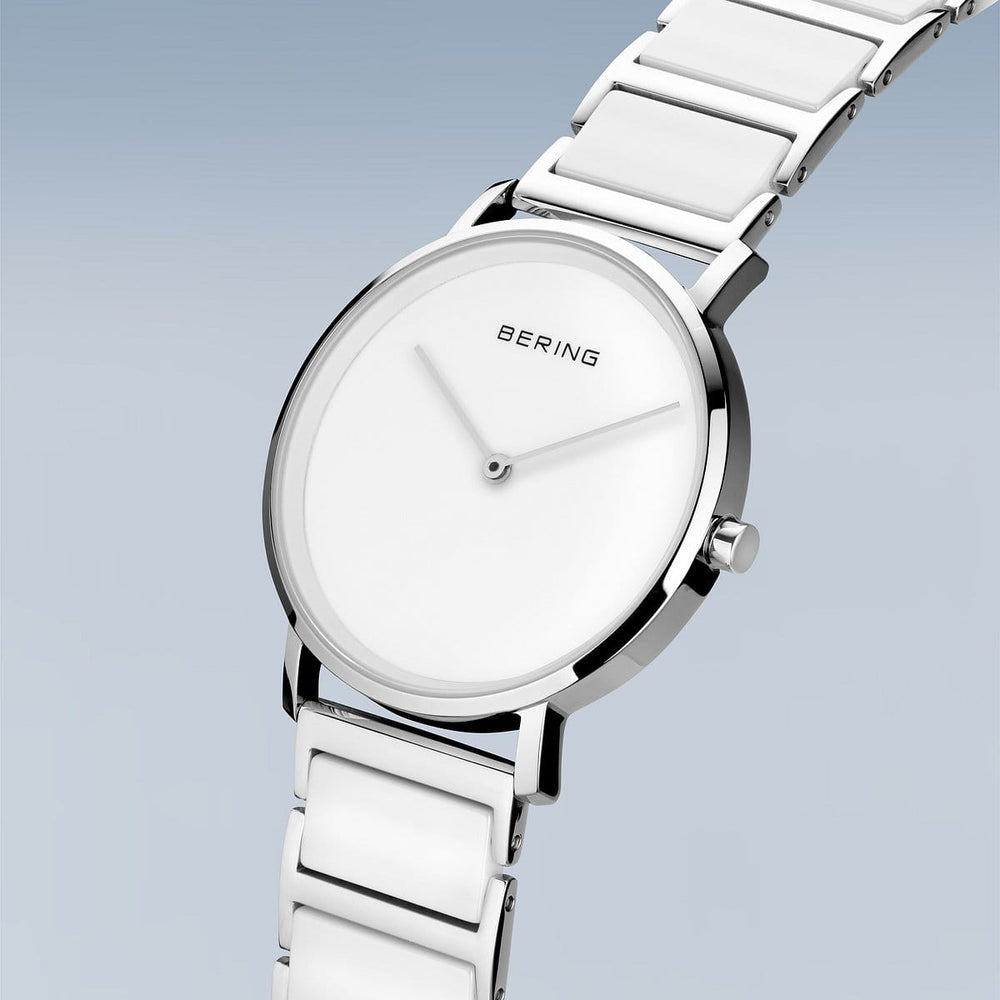 Het Bering dameshorloge, model 18535-754, heeft een strak design met een witte dial, roestvrijstalen kast en dunne zilveren wijzers aangestuurd door Quartz-technologie. Het wordt geleverd met een bijpassende witte band en toont het Bering-logo elegant op een lichtblauwe gradiëntachtergrond.