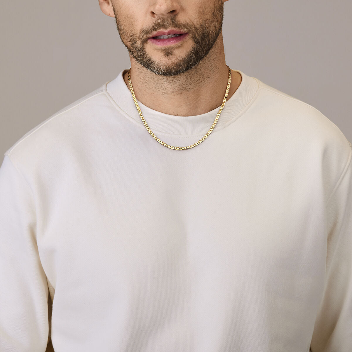 Een man draagt een effen wit sweatshirt en de Van der Kooij Collectie Gouden ketting heren - collier 3,5 mm 14K. Alleen zijn ondergezicht en bovenlichaam zijn te zien tegen een neutrale achtergrond, wat deze verfijnde herenketting benadrukt.