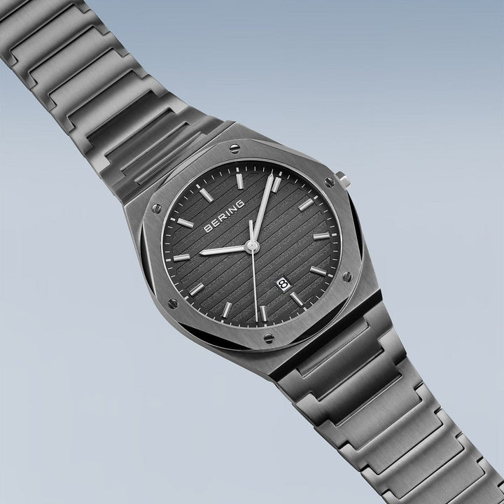 Het Bering Herrenhorloge 19742-777 heeft een roestvrijstalen band en kast, zilveren wijzers, uurmarkeringen, een datumaanduiding op 6 uur en een gestreepte donkergrijze wijzerplaat op een lichtblauwe achtergrond met duurzaam saffierglas.