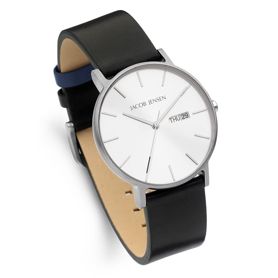 De Jacob Jensen 160 is een minimalistisch quartzhorloge met een strakke zwarte leren band, zilveren kast en witte wijzerplaat met slanke zilveren uurmarkeringen en wijzers. Het heeft een datumvenster op 3 uur met de weergave THU 21.