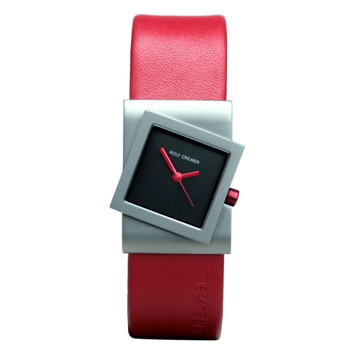 Het Rolf Cremer Horloge 491818 is een modern unisex horloge met een rode leren band, zilveren gekanteld vierkant frame, zwarte wijzerplaat met rode wijzers en markeringen, en Rolf Cremer in het wit. Het heeft een strakke titanium kast en quartz uurwerk.