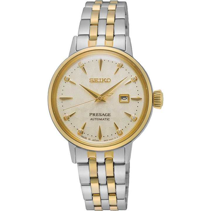 De Seiko Presage dames horloge SRE010J1 van Seiko heeft een automatisch uurwerk, goud-zilveren metalen band, gouden bezel, crèmekleurige wijzerplaat, gouden uurmarkeringen, datumvenster op 3 uur en drie gouden wijzers.