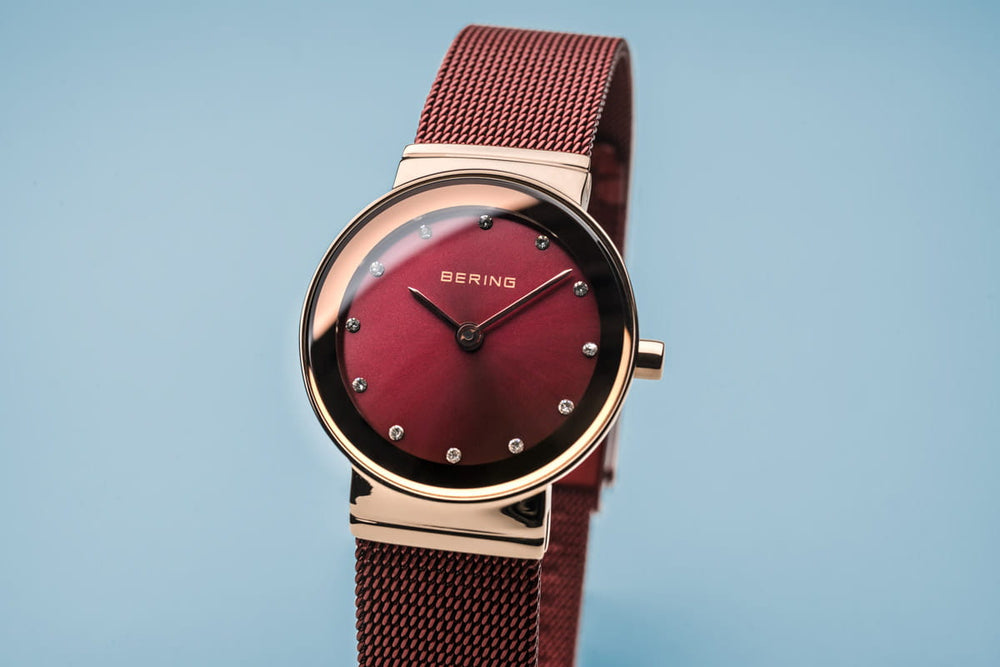 Close-up van het Bering Dameshorloge 10126-363 met een kast van roségoud, een kast van roségoud, een kast van mesh, minimalistische uurmarkeringen en een duurzaam quartz uurwerk van saffierglas tegen een lichtblauwe achtergrond.