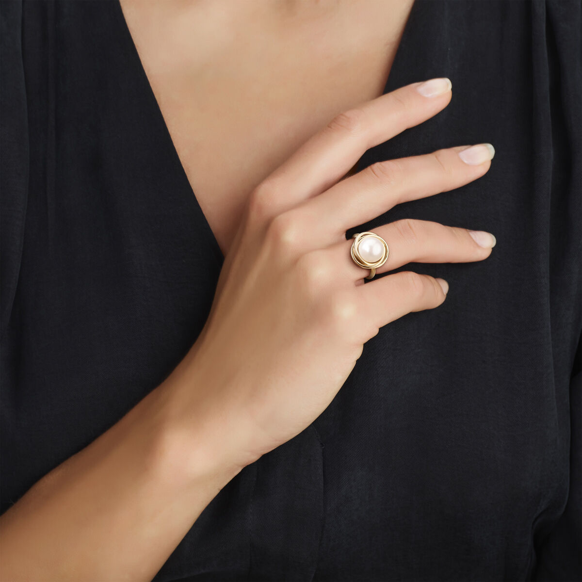 Een persoon in een donker V-hals topje showt de Van der Kooij Collectie ring parel 14K geelgoud met een grote witte zoetwaterparel aan de ringvinger, de hand zachtjes rustend op de borst.