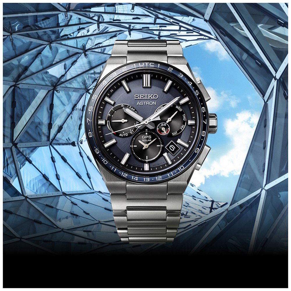 Het Seiko Astron herenhorloge SSH109J1, met een zwart-blauwe wijzerplaat met extra markeringen, versterkt door stevig saffierglas, staat tegen een moderne architectonische achtergrond van glas- en metaalstructuren onder een glimp van de blauwe lucht.