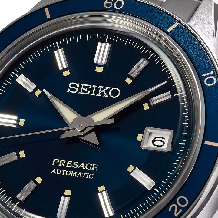 Close-up van een Seiko Prospex heren horloge SRPG05J1 met een blauwe wijzerplaat. Witte wijzers en uurmarkeringen zijn zichtbaar, met de datum op 6 uur. De lunette heeft minutenmarkeringen en Presage Automatic staat boven de 6 uur positie op dit elegante uurwerk.