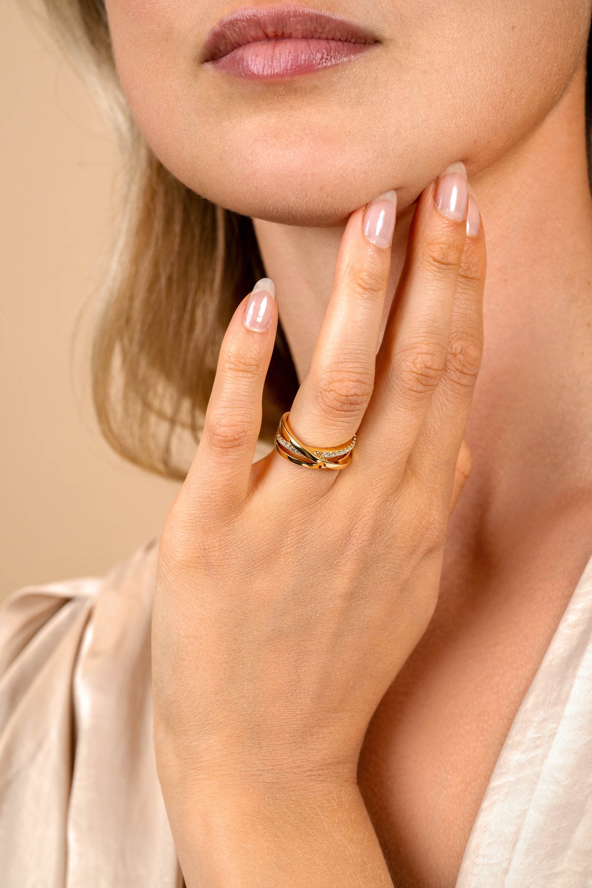 Een vrouw met een lichte huid raakt haar kin aan en toont de Zinzi Ring Gold Plated ZIR1774Y om haar vinger. Haar nagels zijn bleek en netjes en ze draagt een crèmekleurige zijden blouse van Zinzi. Haar lippen zijn lichtjes gespleten.