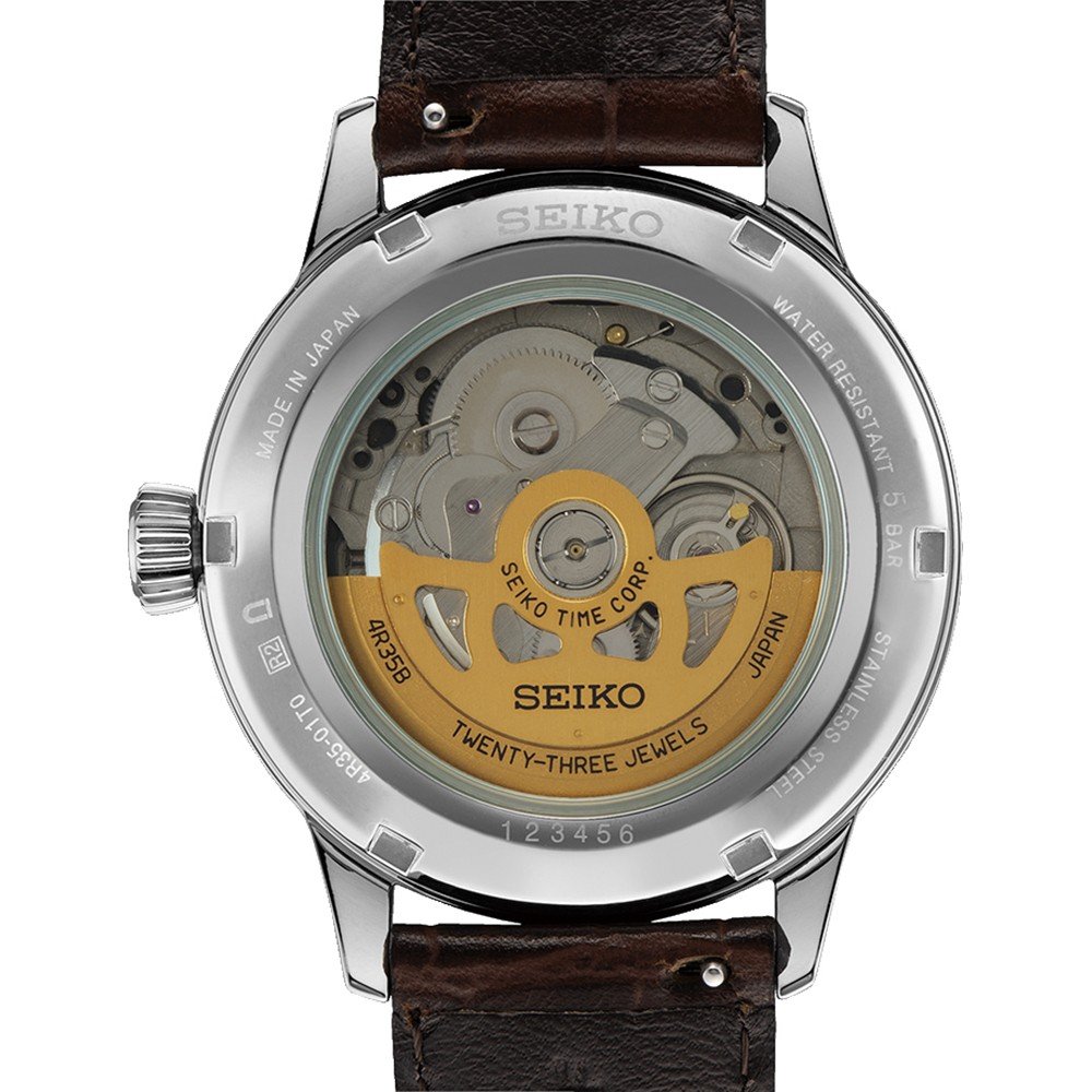 De afbeelding toont de achterkant van een Seiko Presage heren horloge SRPK15J1 met een transparante behuizing, die ingewikkelde mechanica onthult. Seiko Time Corp. Twenty-three jewels staat gegraveerd op de zichtbare rotor van dit automatische horloge, dat een bruine leren band heeft.