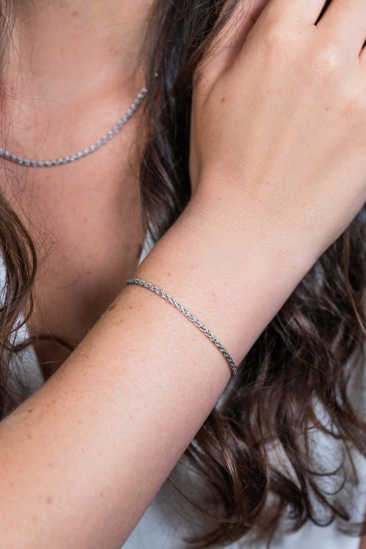 Een persoon met lang bruin haar draagt een elegante zilverkleurige armband vergelijkbaar met de Zinzi Armband Zilver Zia1931 en een bijpassende ketting. Hun hand is bij hun nek, gekleed in een wit topje.