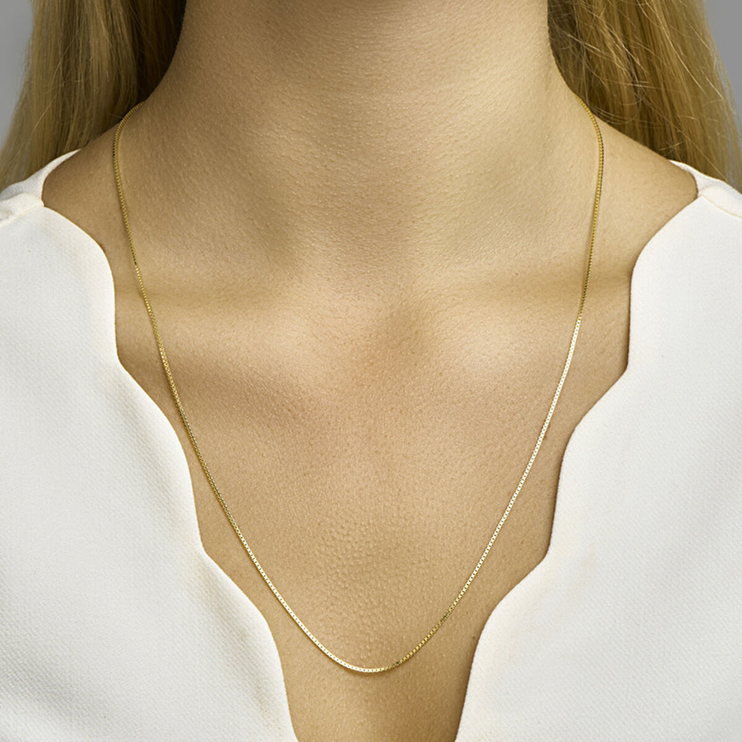 Een close-up van een vrouw die het Van der Kooij Collectie collier venetiaans 1,1 mm 14K geelgoud draagt met een witte blouse met schelpvormige randen, waardoor haar hals, sleutelbeen en een deel van haar borst zichtbaar zijn.