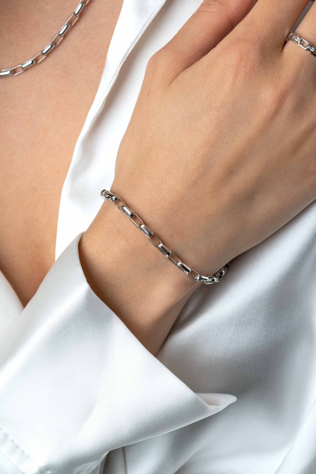 Close-up van een hand met de Zinzi Armband zilver ZIA2514 en ring, met bijpassende ketting, gecombineerd met een wit zijden overhemd.
