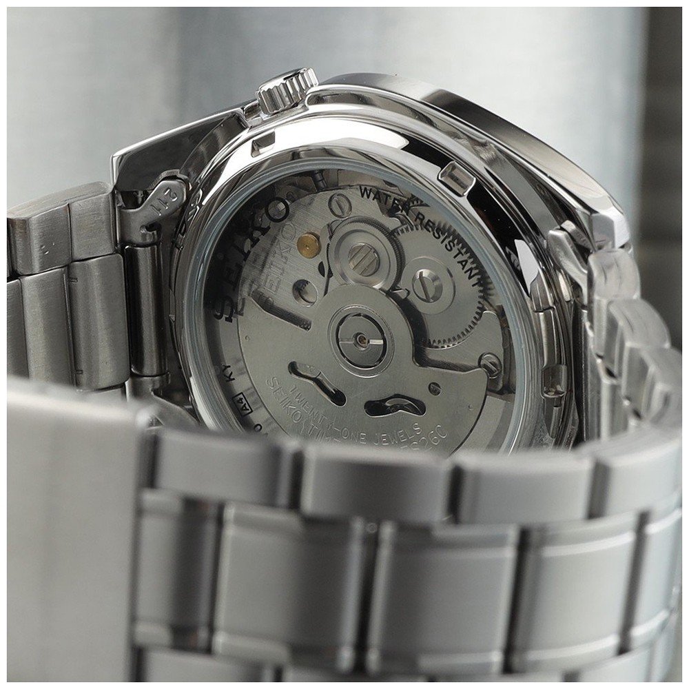 Close-up van het Seiko herenhorloge SNKL45K1, met een gedeeltelijk transparante roestvrijstalen kast die het ingewikkelde automatische uurwerk binnenin onthult. De gepolijste metalen armband staat prominent op de voorgrond.