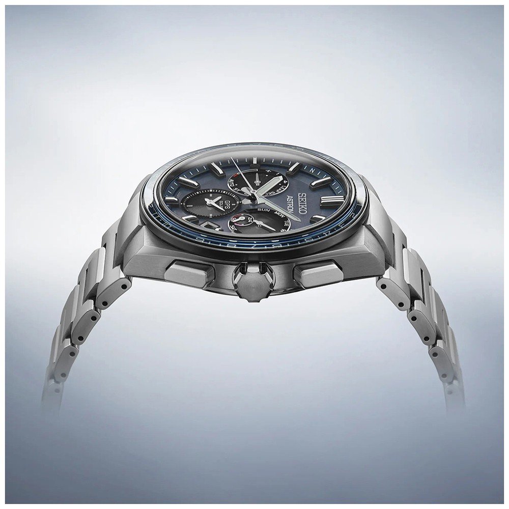 Zijaanzicht van het gestroomlijnde Seiko Astron SSH109J1 herenhorloge, met een zilveren design, donkerblauwe wijzerplaat met subdials en tachymeter. Het beschikt over saffierglas en metaalachtige glans tegen een zachte gradiëntachtergrond, wat de verfijnde stijl benadrukt.