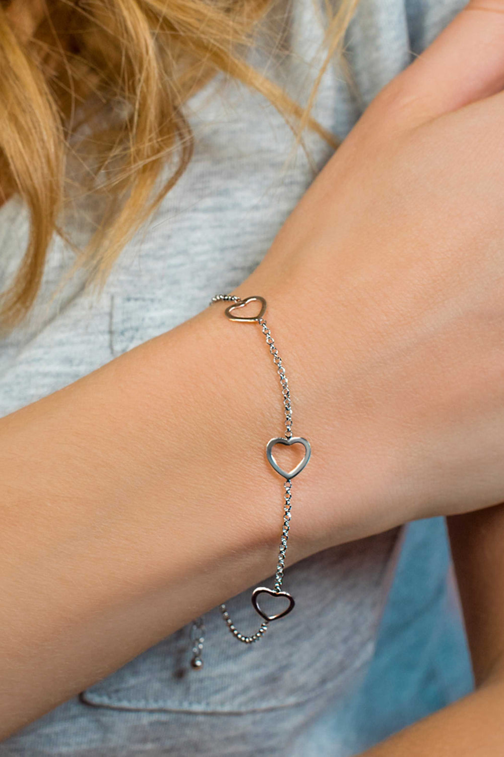 De Zinzi Armband Zilver Zia1188 met delicate hartvormige schakels siert de pols van een persoon. Het elegante stuk, met een afmeting van 17-20 cm, verbetert hun lichtgrijze bovenkant, terwijl lichtbruin haar charme toevoegt aan het ensemble.