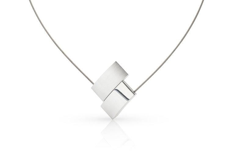 De Collier V-vorm C201 van CLIC Creations is een minimalistische zilveren ketting met twee in elkaar grijpende rechthoekige hangers aan een dunne draadketting. Handgemaakt in Nederland, het unieke ontwerp steekt elegant af tegen een effen witte achtergrond.