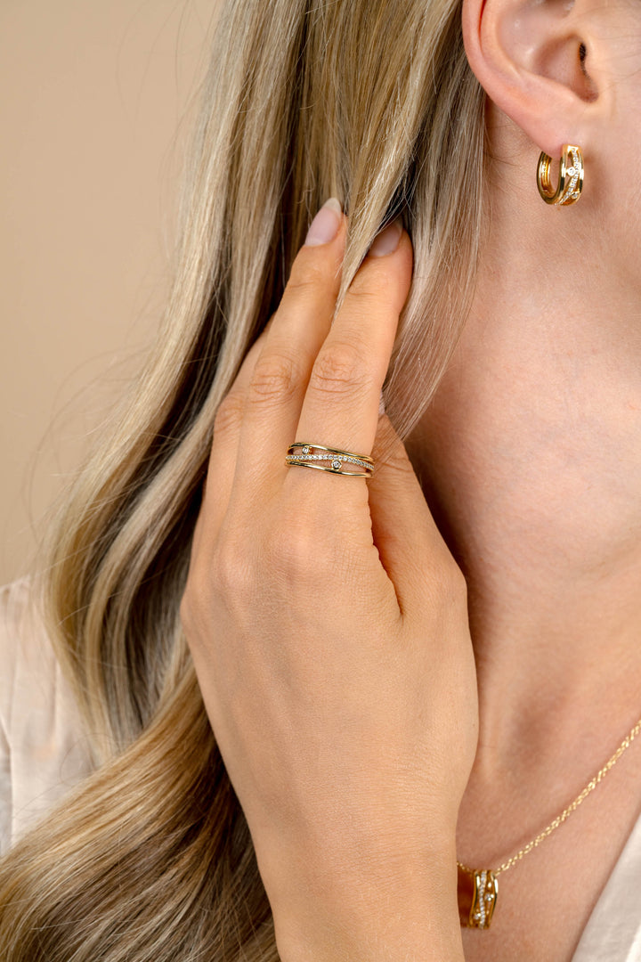 Een blonde vrouw toucheert haar haar bij haar oor, accentueert gouden oorbellen, een delicate gouden ketting en de Zinzi Ring Zilver ZIR2685 van Zinzi.