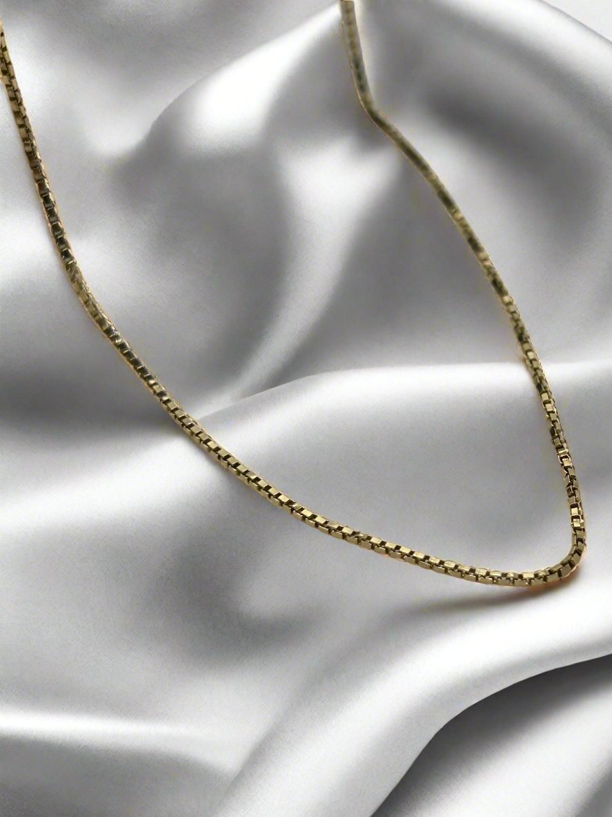 Het vintage gouden collier 45cm 14K venetiaans 3.2gr van Juwelier van der Kooij versterkt de gladde, witte satijn met een zacht, elegant contrast tussen het glanzende goud en de zijdezachte stof.