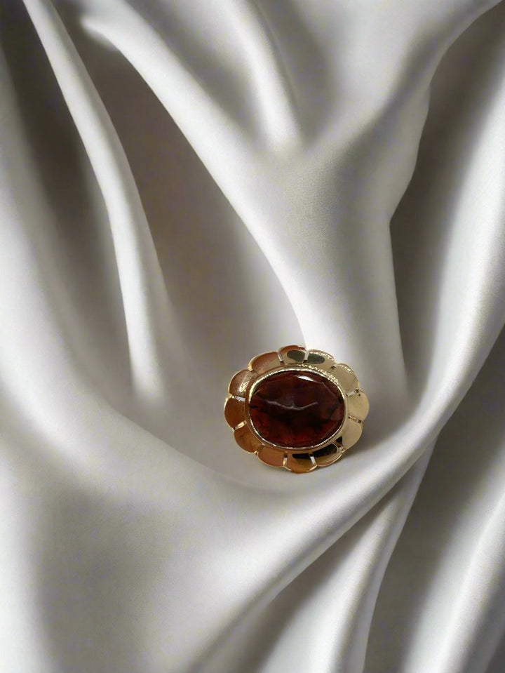 Een vintage gouden ring 14k ovale kwarts 3.5gr van Juwelier van der Kooij rust op een gladde, vloeiende witte stof, waardoor een opvallend contrast ontstaat tussen de levendige sieraden en de zachte achtergrond.