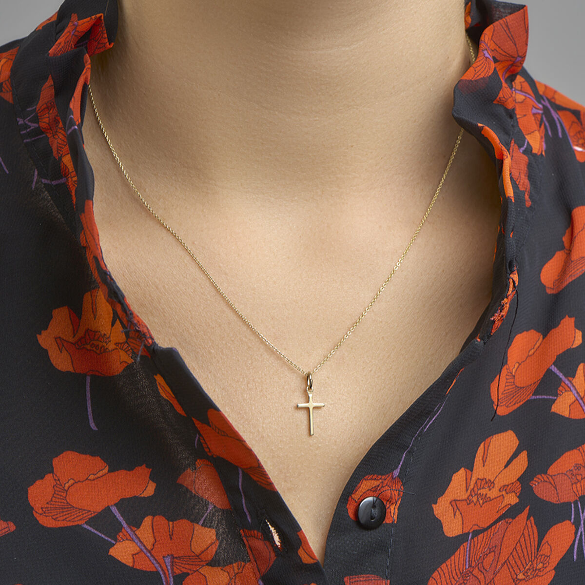 Close-up van een persoon die de Van der Kooij Collectie hanger kruis 3 micron zilver verguld (geel) draagt en een zwarte blouse met een rood en oranje bloemenpatroon en een geplooide kraag, die bij de hals iets open is.