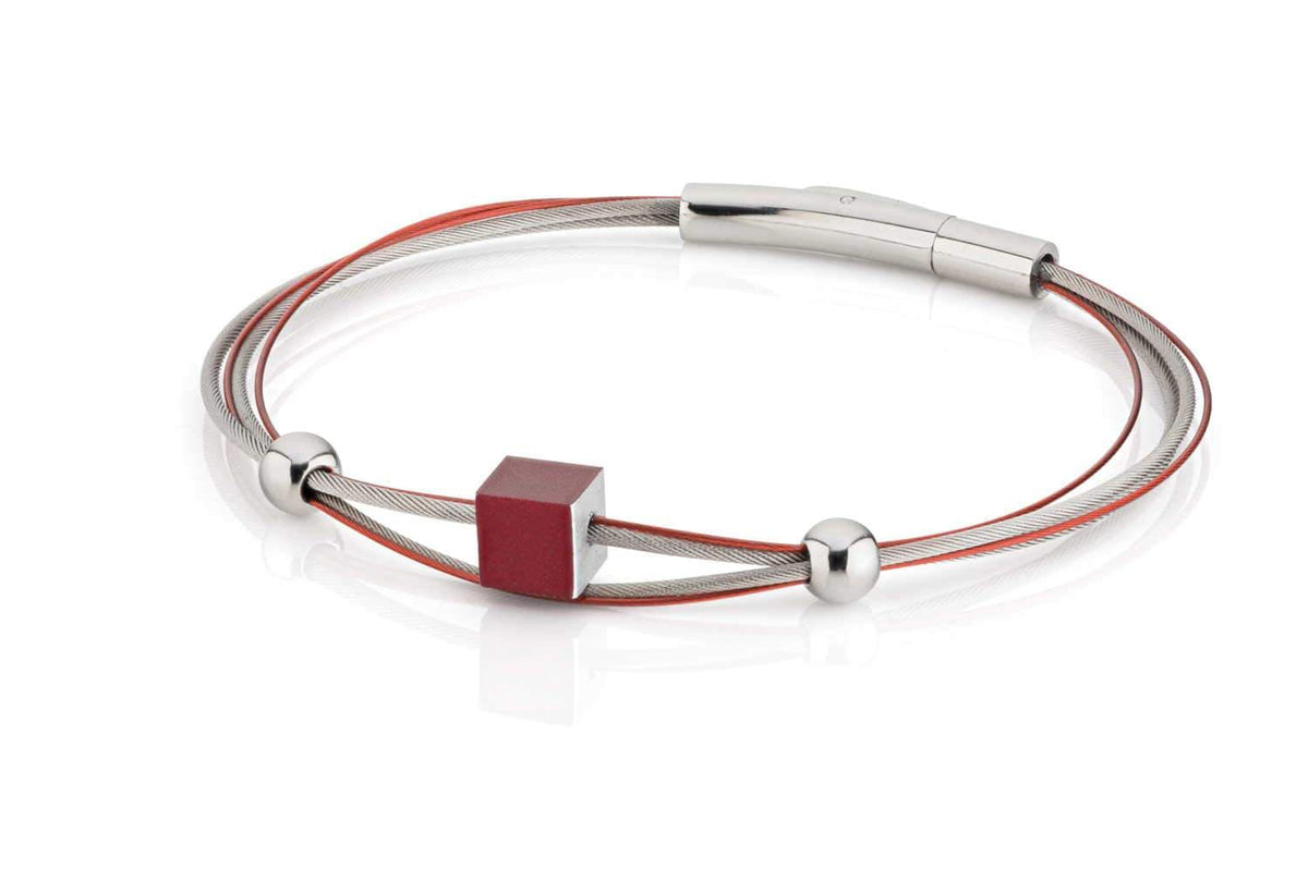 Pulsera con un cubo rojo y detalles metálicos, formada por hilos de acero y esferas brillantes.