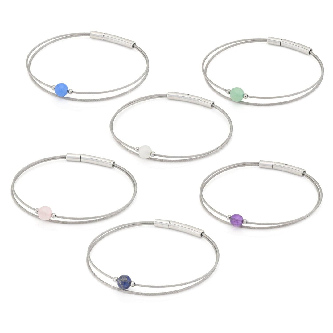 De Thinking of You armband Aquamarijn zilver A721B van CLIC Creations heeft zes elegante zilveren draad bangles, elk met een unieke gekleurde kraal: blauw, groen, wit, roze, donkerblauw en paars. Hun minimalistische ontwerp omvat een cilindrische sluiting en ze zijn gerangschikt in twee rijen van drie.
