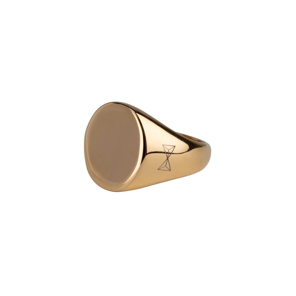 Anillo signet dorado con superficie lisa y detalle grabado en un lateral.