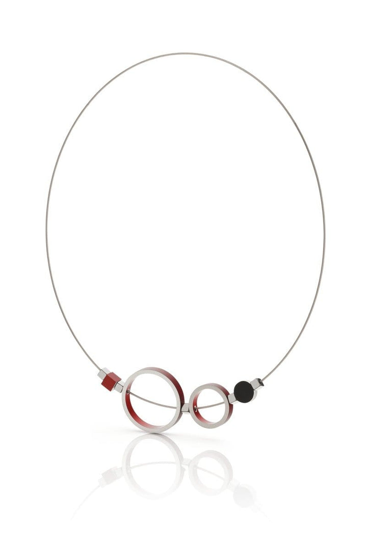 De Collier Ringen Rood C186R van CLIC Creations is een minimalistische ketting met dun zilverdraad met twee kruisende cirkels als hanger - één grotere en rode, één kleinere en zwarte - plus een klein rood vierkant en een zwarte cirkel op de draad voor een unieke elegantie.
