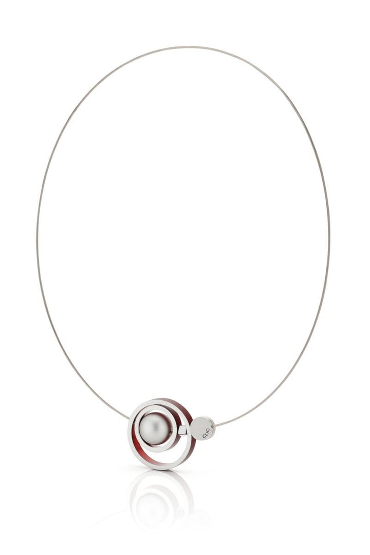 De Collier Ringen in elkaar Rood C187R van CLIC Creations is een minimalistische ketting die met de hand is gemaakt in Nederland, met een slanke ronde draad met een hanger van een bolvormige zilveren kraal en twee concentrische ringen, een rode en een zilveren. Het wordt elegant gepresenteerd tegen een effen witte achtergrond.