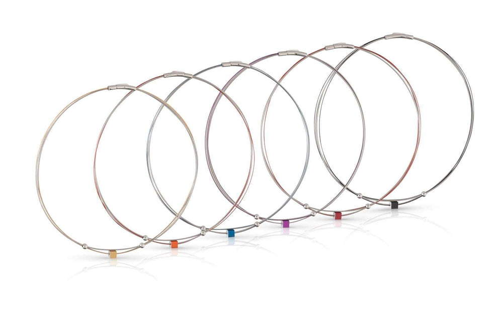 Zeven dunne metalen kabel sleutelhangers van CLIC Creations, genaamd Collier Klein Kubusje Oranje C230O, staan op een rij. Ze hebben elk een kleine kubus met gekleurde labels: geel, oranje, rood, paars, blauw, groen en zwart. De edelstalen bajonet sluiting zorgt voor een veilige pasvorm en glanzende afwerking.