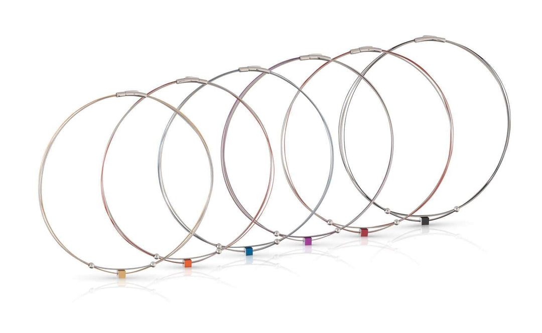 Zeven dunne metalen kabel sleutelhangers van CLIC Creations, genaamd Collier Klein Kubusje Oranje C230O, staan op een rij. Ze hebben elk een kleine kubus met gekleurde labels: geel, oranje, rood, paars, blauw, groen en zwart. De edelstalen bajonet sluiting zorgt voor een veilige pasvorm en glanzende afwerking.