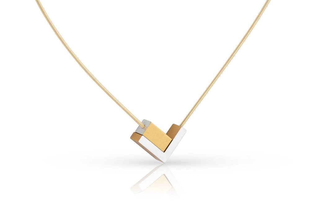 De CLIC Creations Collier V-tje met en rechthoekje Goud|Geel C256G heeft een gouden en zilveren geometrische hanger aan een edelstalen collier draad. Het V-vormige ontwerp biedt een strakke, moderne look, waarbij de hanger elegant hangt aan een dunne gouden ketting, die subtiel het licht eronder reflecteert.